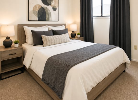A bedroom with a large bed, a painting on the wall, and two lamps on the nightstand.