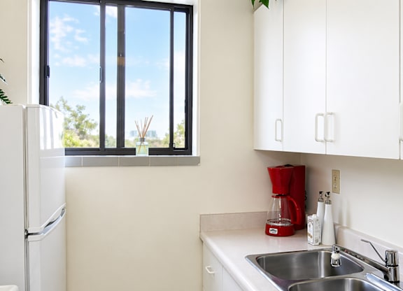 A kitchen with a white fridge, white cabinets, and a window.