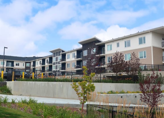 A row of modern townhouses with a concrete wall and greenery in the foreground.