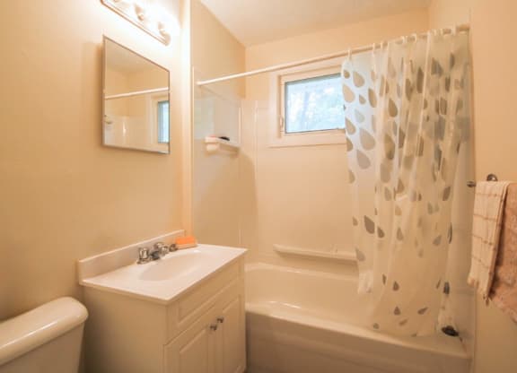 A white bathroom with a sink, mirror, and bathtub.