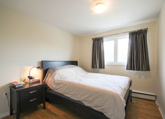 A bedroom with a bed, nightstand, and window.