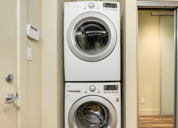 A white front load washing machine is stacked on top of another in a small room.