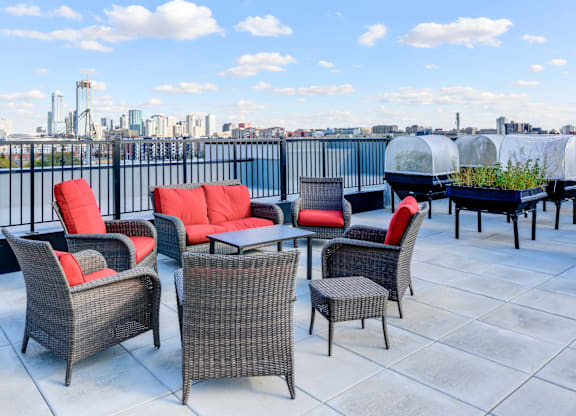 A patio with red cushions and grey wicker furniture overlooking a city skyline.
