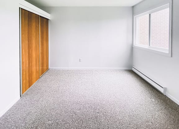 A room with a carpeted floor and a window with blinds.