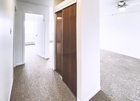 A hallway with a carpeted floor and a ceiling fan.