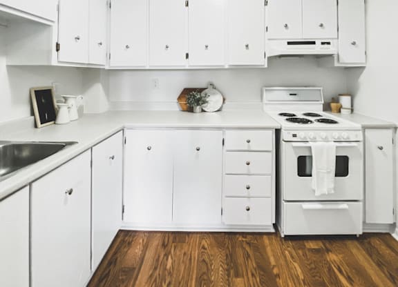 A white kitchen with wooden floors and a stove top oven.