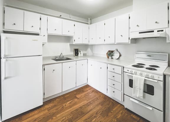 A white kitchen with wood floors and white appliances.