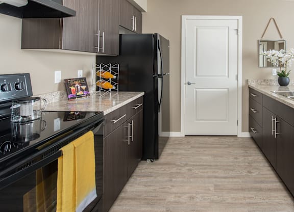 A black refrigerator stands in a kitchen with wooden cabinets and a white door.
