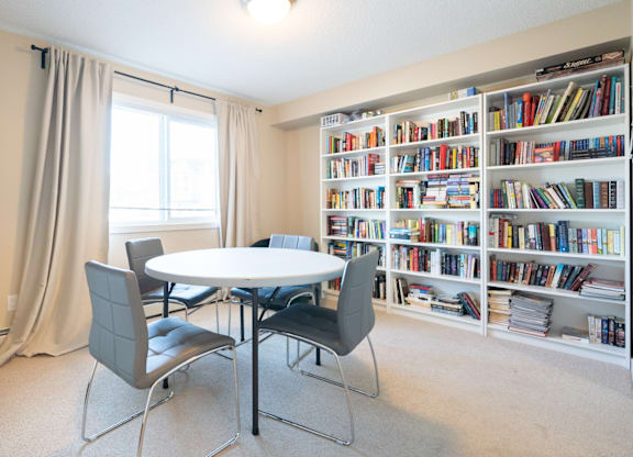 A room with a table, chairs, and a bookshelf filled with books.