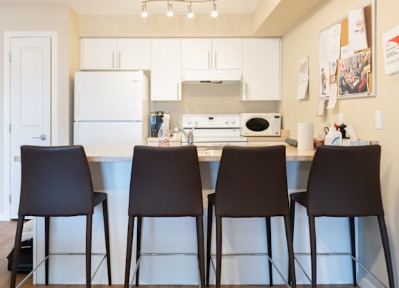 A kitchen with white appliances and brown chairs.