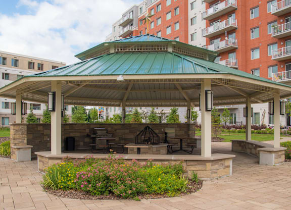 A gazebo with a green roof is surrounded by a brick patio and flowers.