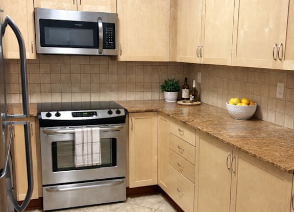 A kitchen with a stainless steel oven and microwave above a counter with a bowl of lemons on it.