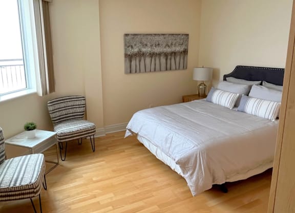 A bedroom with a bed, chair, and painting on the wall.
