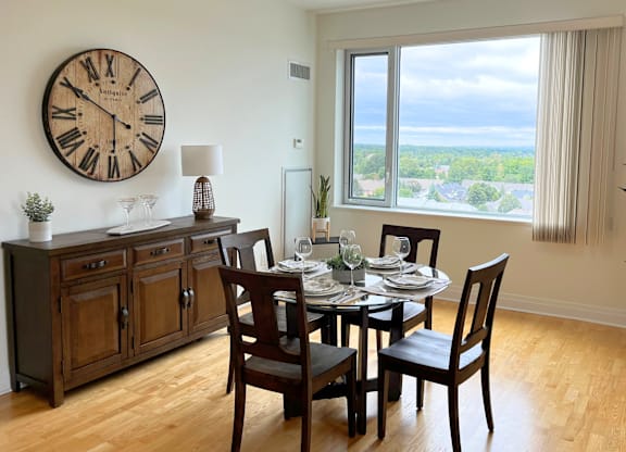 A dining room with a table set for four and a large clock on the wall.