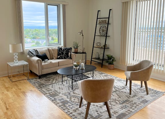 A living room with a couch, two chairs, a table, and a large window with a view of the ocean.
