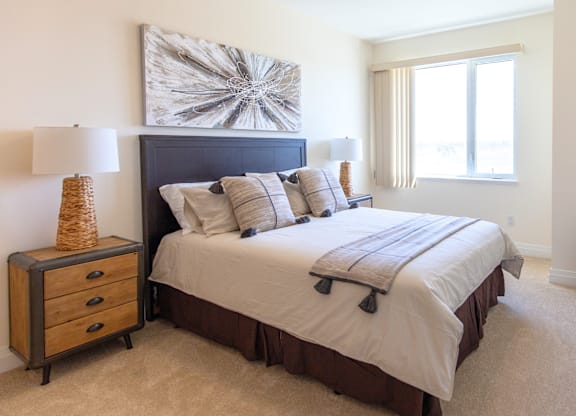 A bedroom with a large bed, a nightstand with a lamp, and a painting on the wall.