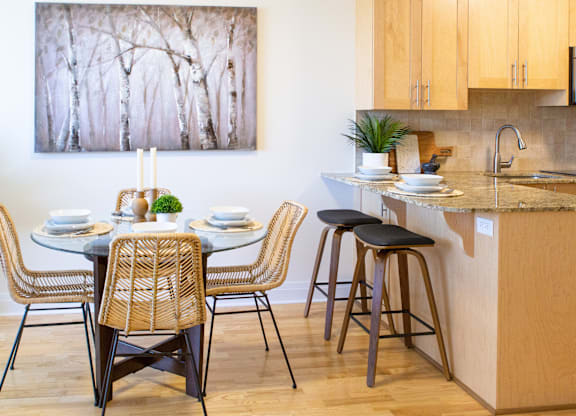 A kitchen with a table set for two and a painting of trees on the wall.