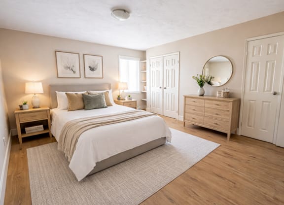 A bedroom with a large bed, a nightstand with a lamp, and a dresser with a mirror.