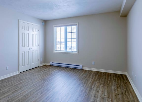 A room with a white door, a window, and a wooden floor.