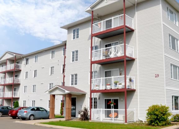 A white apartment building with red balconies and a car parked in front.