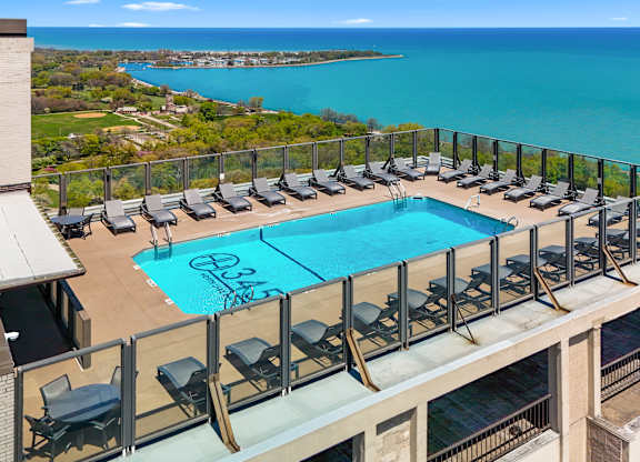 A pool with lounge chairs is surrounded by a balcony railing.