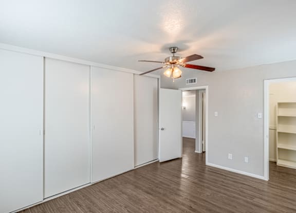 A room with a ceiling fan and a row of white cupboards.