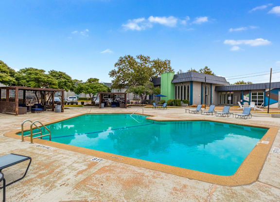 A large outdoor swimming pool surrounded by lounge chairs and trees.