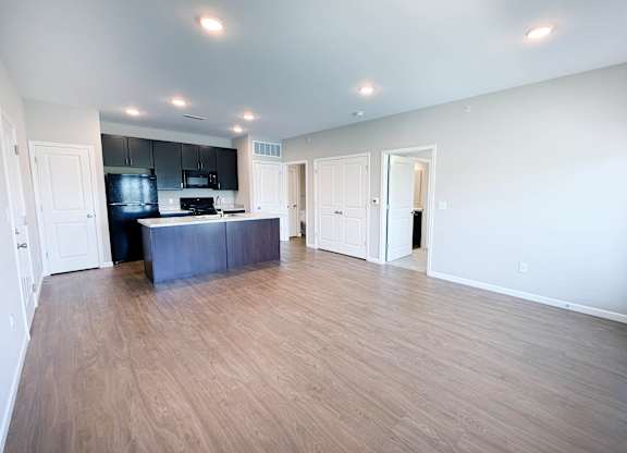 A spacious room with wooden flooring and a kitchen area with black cabinets.