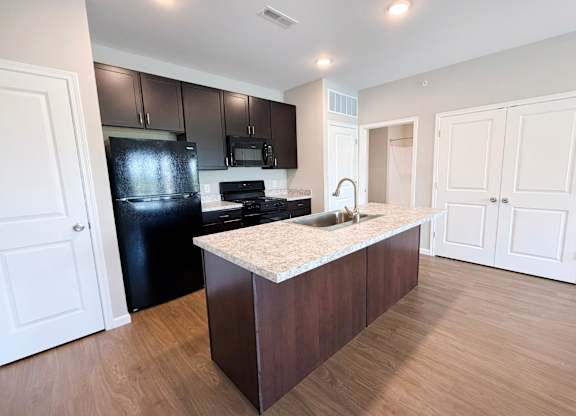 A kitchen with a black refrigerator and stove top oven.