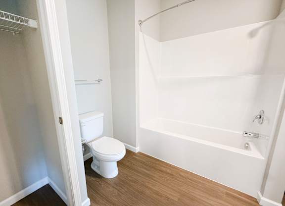 A white toilet sits in a small bathroom with a white tub.