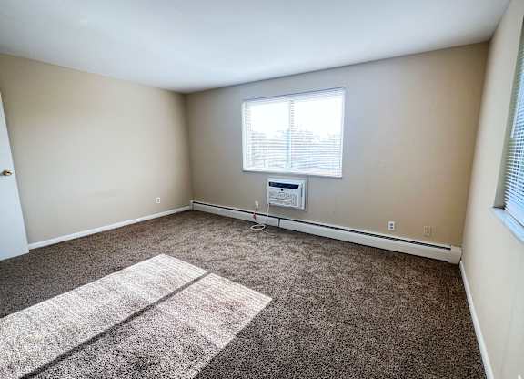 A room with a carpeted floor and a window with blinds.