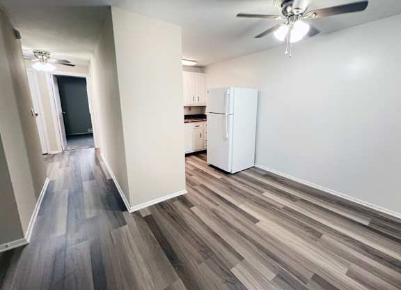A room with a white fridge and a ceiling fan.
