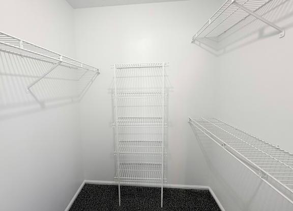 A walk-in closet with white shelving and a black carpeted floor.