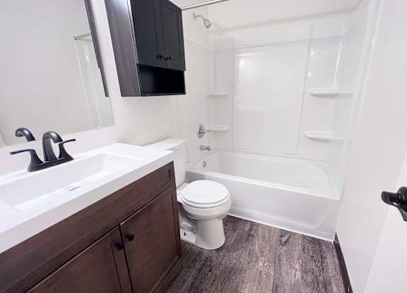 A white toilet sits in a bathroom next to a sink and a bathtub.