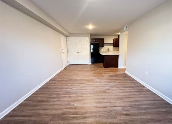 A long, empty room with wooden flooring and white walls.