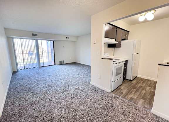 A spacious living area with a kitchenette and a sliding glass door leading to a balcony.