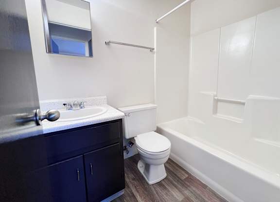 A white toilet sits in a bathroom with a white sink and a white bathtub.