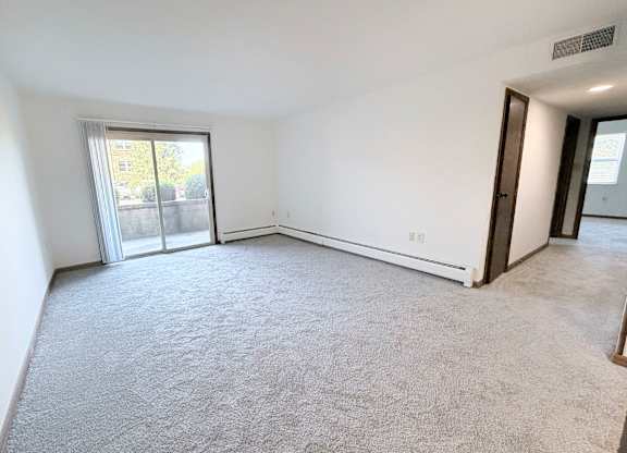 A spacious room with a carpeted floor and sliding glass doors leading to a balcony.