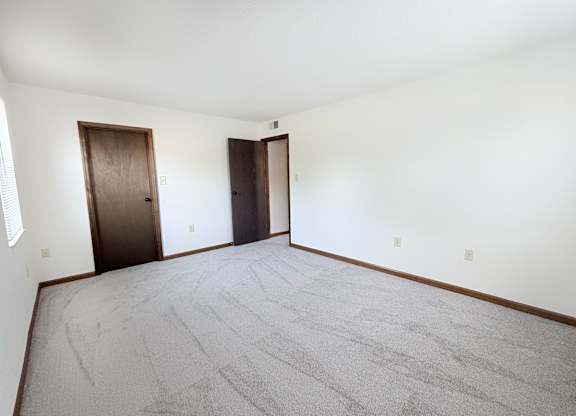 A room with a carpeted floor and two doors.