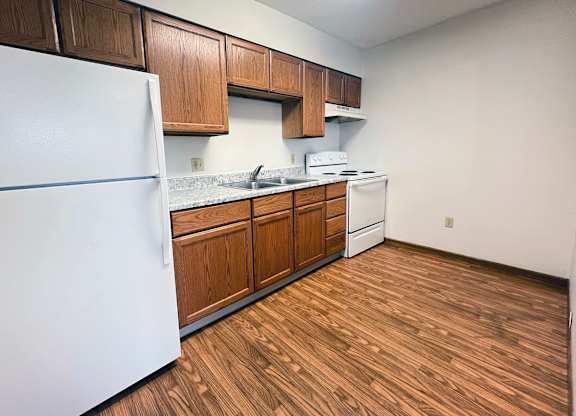 A kitchen with a white fridge, wooden cabinets, and a white stove top oven.