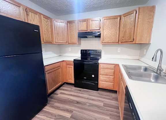 A kitchen with a black fridge and wooden cabinets.