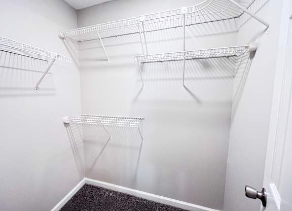 A white walk in closet with shelves and a black carpet.