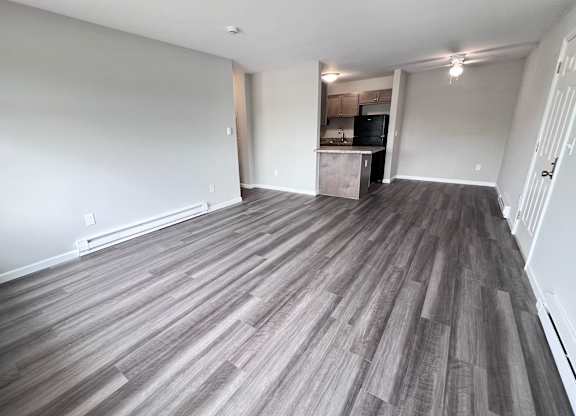 A room with a wooden floor and a kitchen in the background.
