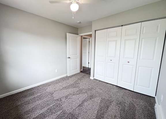 A room with a grey carpet and white cupboards.