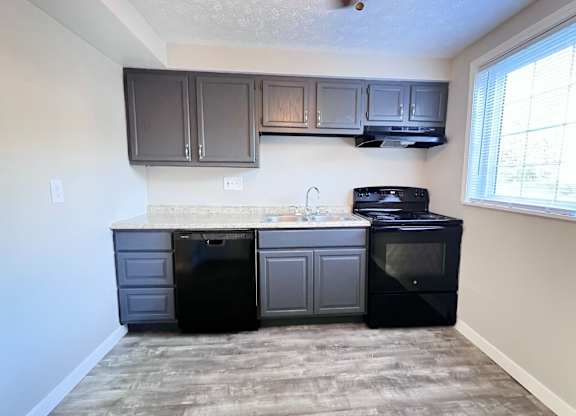A kitchen with black appliances and grey cabinets.