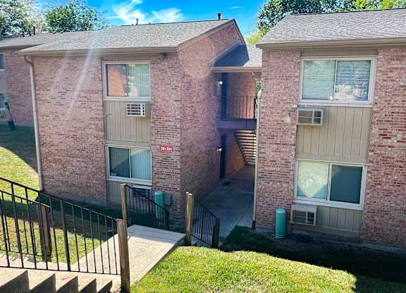 A brick apartment building with a black railing and a green trash can.