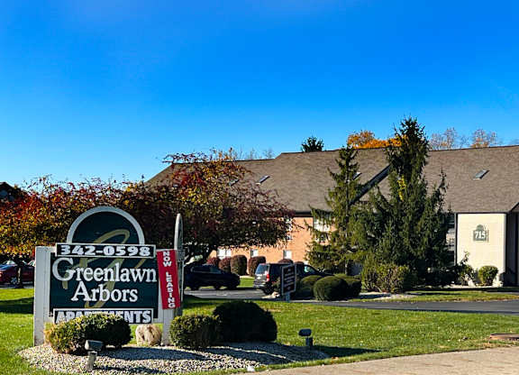 A sign for Greenlawn Arbors apartments is displayed in front of a building.