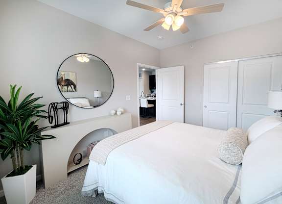 A bedroom with a large bed, a mirror, and a ceiling fan.