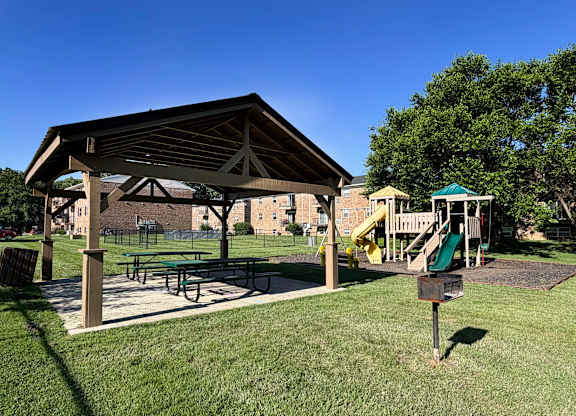 A playground with a wooden pavilion and a green slide.