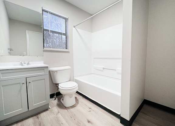 A white toilet sits in a bathroom with a white tub and sink.